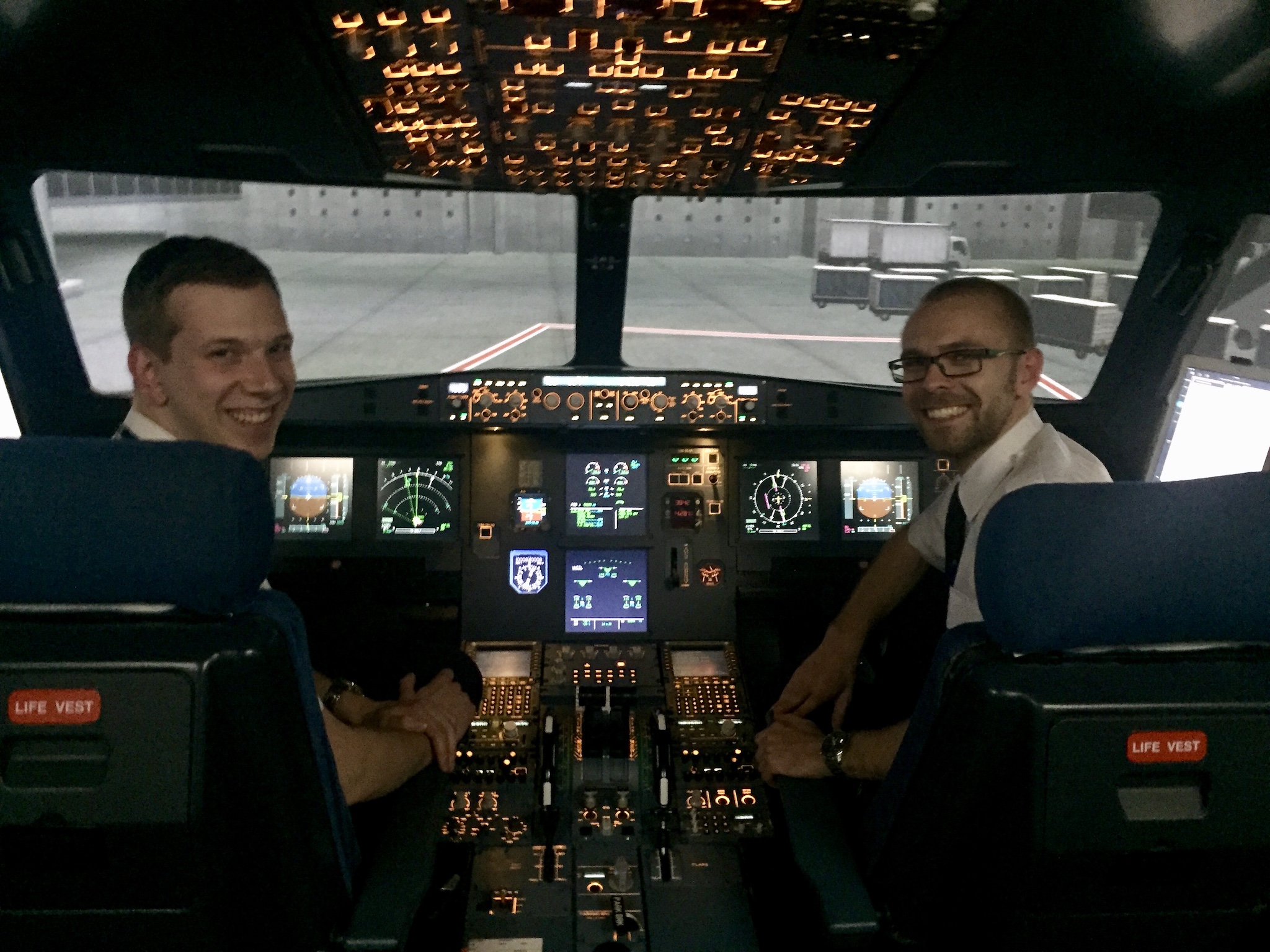 A couple of EPL students smiling at the camera from their seats in the A320 simulator